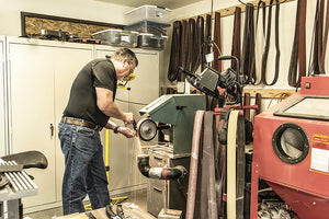 An man in a work shop using a piece of machinery to sharpen a cutting tool with sparks flying.